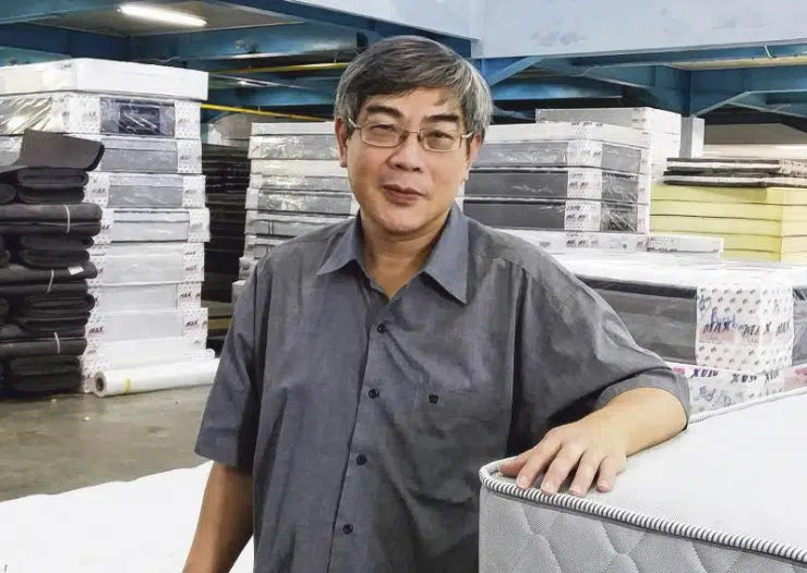 Man standing beside luxury mattress in warehouse, showcasing premium bedding solutions for smart sleep wellness